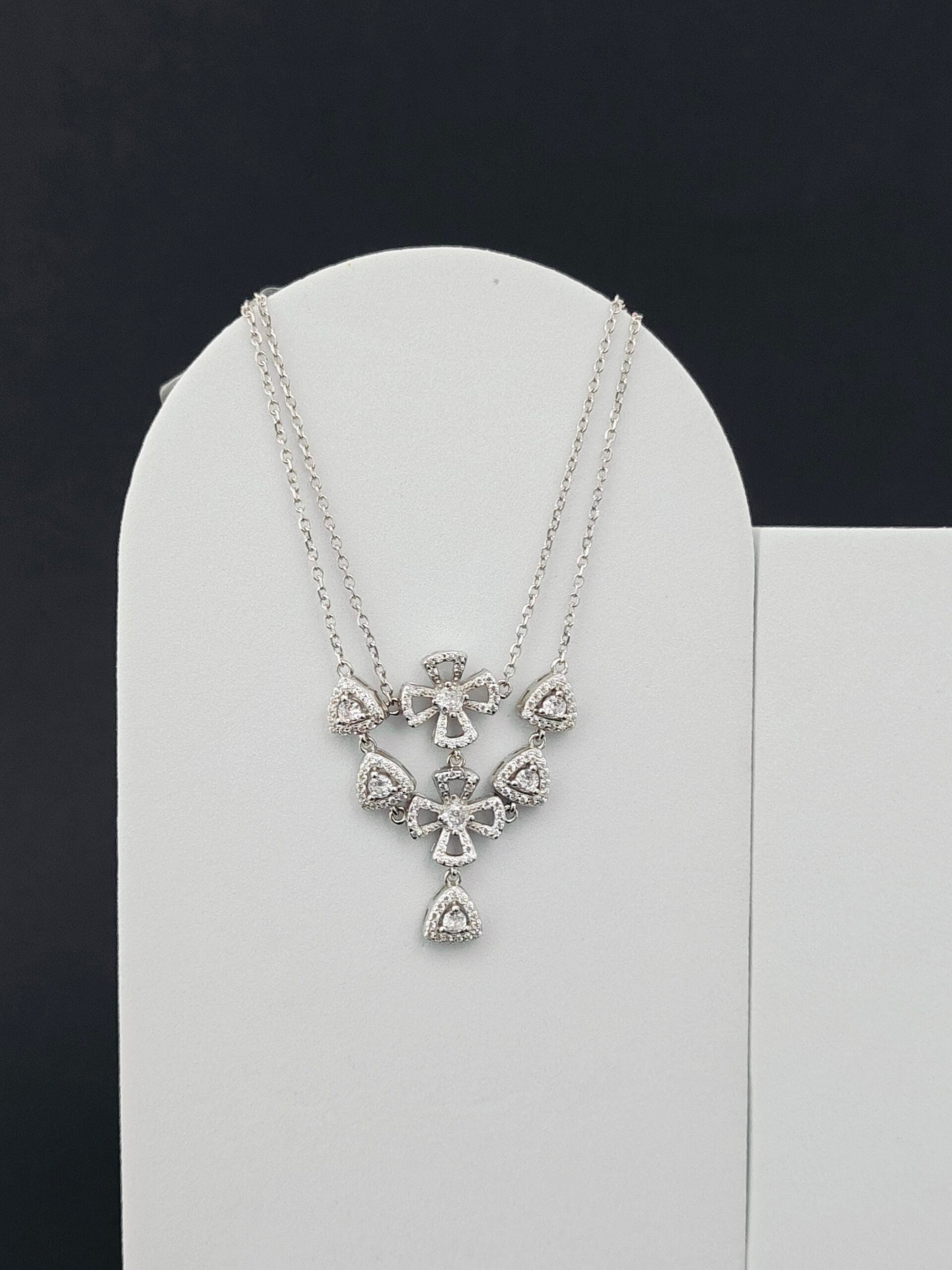 Silver necklace with bow-shaped pendant on a white stand against a black background